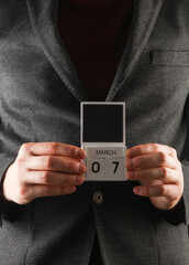 Business man in a jacket holding a calendar with the date March 7