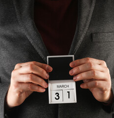 Business man in a jacket holding a calendar with the date March 31