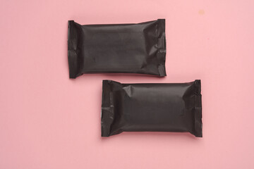 Two black packages of wet wipes on pink background