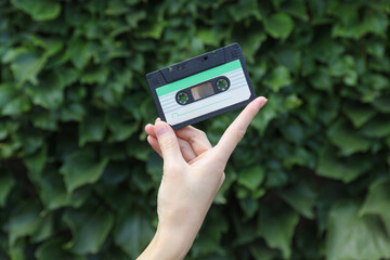 Hand holding retro audio cassette on green leaves wall background
