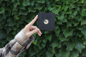 Floppy disk in hand on green leaves wall background