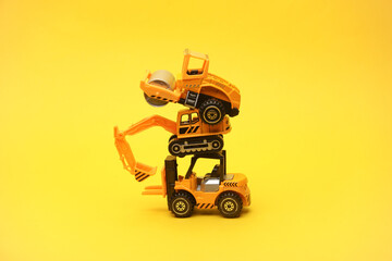 Toy asphalt paver and excavator on yellow background