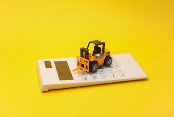 Miniature toy forklift and calculator on a yellow background. Logistics, delivery