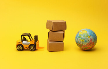 Miniature toy forklift and globe with boxes on a yellow background. Logistics, transportation,...