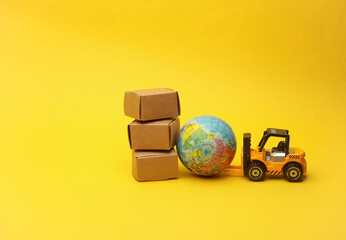 Miniature toy forklift and globe with boxes on a yellow background. Logistics, transportation,...