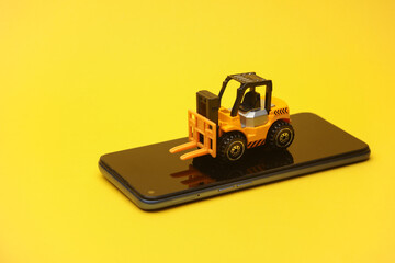 Miniature toy forklift and smartphone on a yellow background. Logistics, transportation, delivery