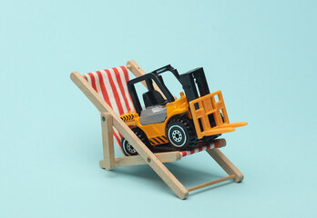 Miniature toy forklift and deck chair on blue background. Logistics, vacation concept © splitov27