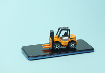 Miniature toy forklift and smartphone on a blue background. Logistics, transportation, delivery