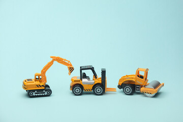 Toy forklift, asphalt paver and excavator on blue background - obrazy, fototapety, plakaty