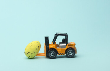 Miniature toy forklift and easter egg on a blue background.