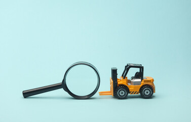 Miniature toy forklift and magnifying glass on blue background. Logistics, transportation, delivery © splitov27