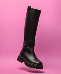 High leather women's black boots levitate on a pink background. Minimal fashion concept
