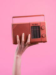 Female hand holding a pink retro radio receiver on a pink background