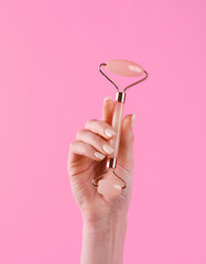 Woman's hand holds a massage jade facial roller on a pink background. Anti-aging therapy