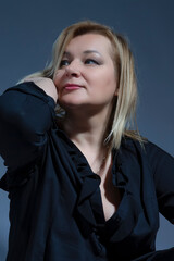 One Sitting Sensual Alluring Mature Confident Caucasian Woman in Black Shirt With Lifted hand Near Face On Dark White