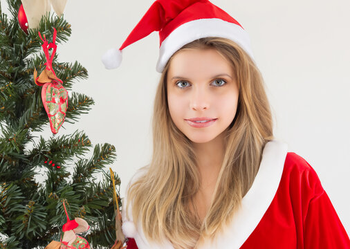 クリスマスのイメージの人物写真、クリスマスツリー、サンタクロースの衣装と、帽子をかぶった若い笑顔の白人女性　白背景