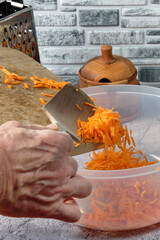 a chef's hand with a wooden spatula unloads grated carrots into a plastic bowl