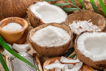 Fresh opened coconuts along with coconut slices, flakes and coconut leaves on a wooden table.