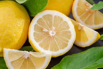 Ripe lemon fruits with slices and lemon leaves on a gray stone table.