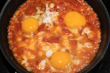 Shakshouka cooking in iron pan top view.