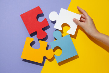Colored paper puzzles and hand on yellow and purple background, top view