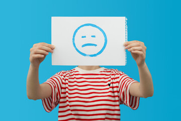 Woman with album sheet with sad emoji on blue background