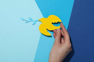 Decorative paper bird in hand on blue background, top view