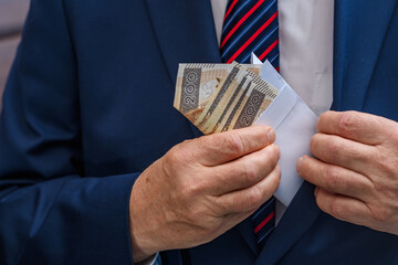 Elegancki mężczyzna chowa kopertę z polskimi banknotami do kieszeni