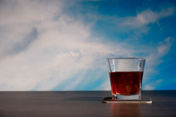 Glass of whiskey on the bar in front of the blur image Cloudscape. Blue sky and white cloud. Sunny day. Cumulus clouds.