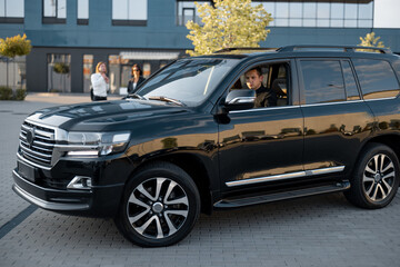 Man drives luxury black SUV vehicle near an office building, side view. Big boss concept