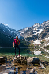 Young woman in red sportswear standing in the nature, mountain lake and range on the background,...
