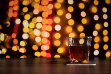 Glass of whiskey on the bar in front of the blur image Christmas home room with tree and festive bokeh lighting, blurred holiday background