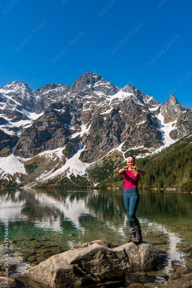 Wall mural a woman stands and shows a heart by a beautiful lake in the mountains. famous mountains lake morskie - Wall murals