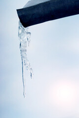 A large icicle hangs from a gutter in winter in sunny weather