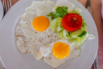 two fried eggs with vegetables on a white plate