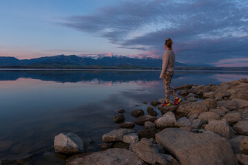 Woman traveler admiring the sunset on the shore of a lake in the mountains.