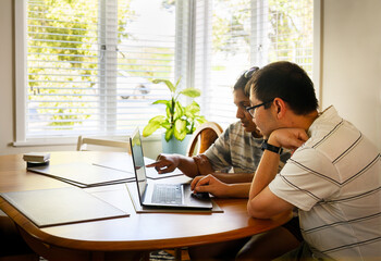 Young couple planning budget, shopping online. Man and Woman looking at laptop screen, sitting at table at home together.