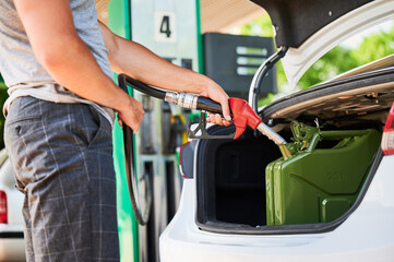 Male driver with gas pump refueling canister with fuel in car trunk. Man holding hose and filling...