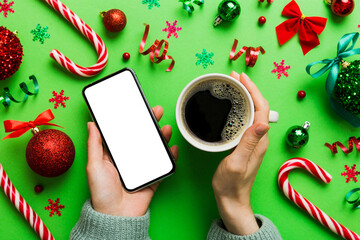 Above view of female hand holding smart phone with hot cup of coffee. Christmas decoration on...