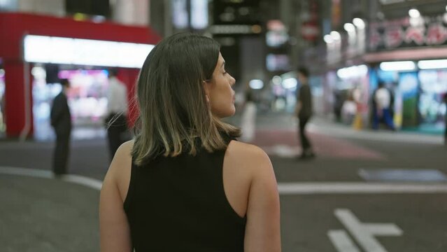 Beautiful hispanic woman walking away, strolling tokyo streets, casting backward glances to cityscape night lights
