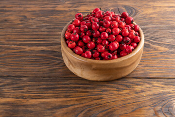 red hawthorn berries in wooden bowl on flat wooden surface