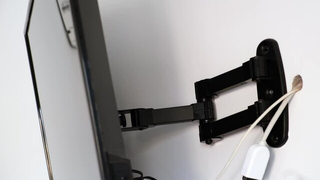 A man rotates a flat-screen TV hanging on a bracket, demonstrating a wide angle of rotation of the screen. The TV bracket demonstration. Mount bracket for LCD monitor, plasma TV, LED display device