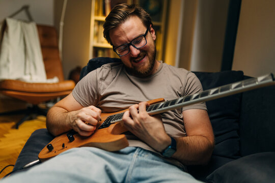 Front view of a happy Caucasian man plying an electric guitar at home.