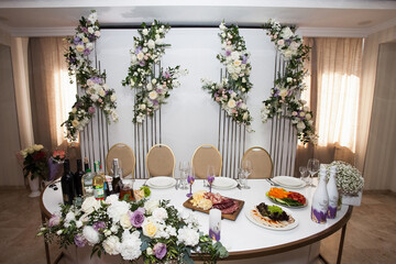 Served table of the newlyweds against the backdrop of a stylish floral decor in the banquet hall. Image on the theme of wedding, banquet and design.