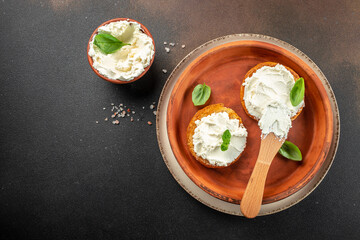 toasted bread with cream cheese and fresh basil leaves on a dark background. top view. copy space...
