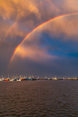 Beautiful double rainbow over the sea and coast full of small private boats right after the storm and rain at beautiful cloudy sunset at golden hour