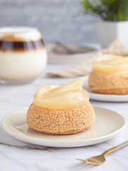 A French cream puff crack bun (Choux au Craquelin) topped with poached pear fruit with glass of latte coffee in background. It's a dessert base of savory choux dough bun and pastry cream