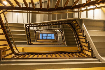 View to top of highlighted high and old square spiral staircase with decorative wooden railings and...