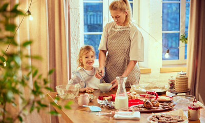Happy family time. Young woman, mother cooking with little girl, daughter in modern kitchen at home. Cooking croissants and cookies. Concept of cookie day, motherhood, childhood, holidays, family