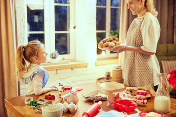Happy smiling young woman carrying prepared cookies and croissants. Little girl, daughter cooking at home. Coziness. Concept of cookie day, motherhood, childhood, holidays, family